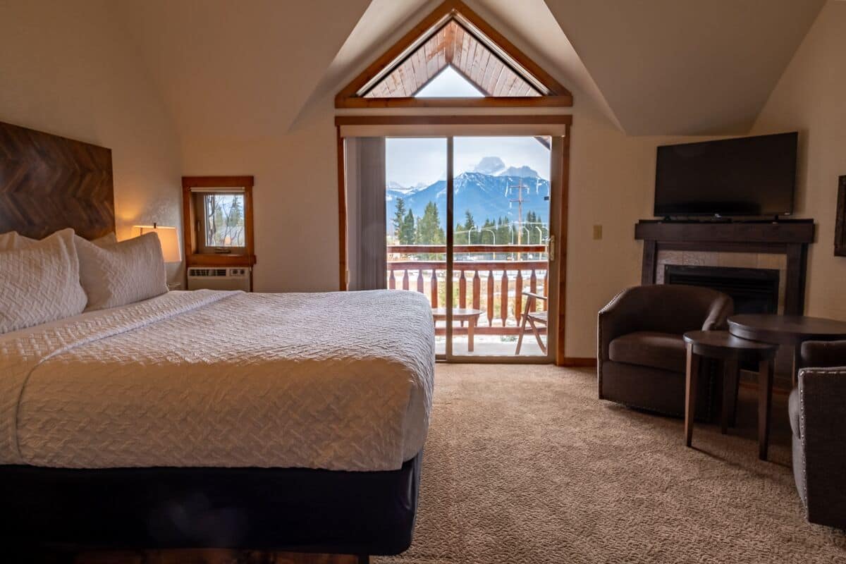A bedroom with a large bed, a TV, a fireplace, and a balcony with a mountain view.