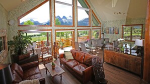 Un salon spacieux avec un canapé en cuir, une table à manger en bois et de grandes fenêtres offrant une vue sur les montagnes.