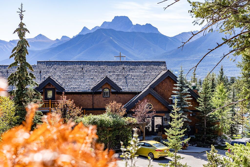 A brick building with a sloped roof, a wooden porch, and a mountain backdrop.
