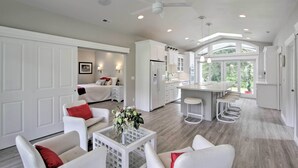 A spacious living area with a kitchen and dining area, featuring white cabinetry, a ceiling fan, and a large window providing natural light. - Contemporary Tacoma Cottage w/ Deck & Pond! (Tacoma)