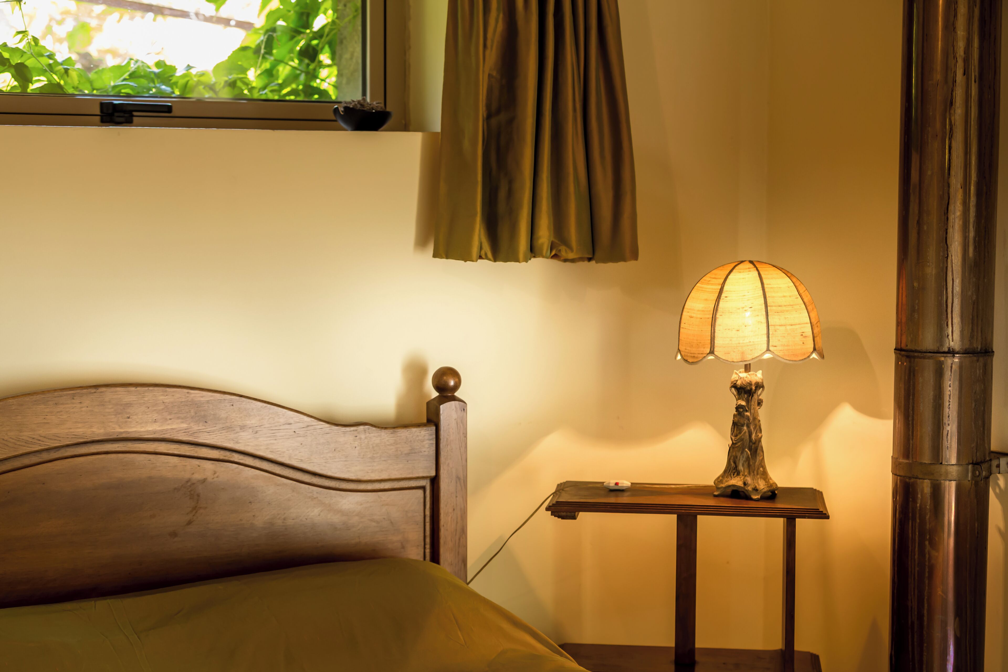 A bed with a wooden headboard, a bedside table with a lamp, and a window with curtains.