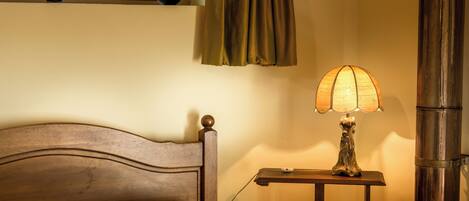 A bed with a wooden headboard, a bedside table with a lamp, and a window with curtains.