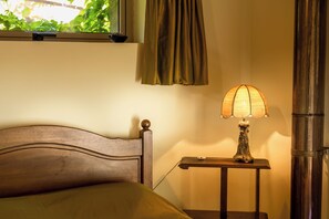 Una cama con cabecera de madera, una mesita de noche con lámpara y una ventana con cortinas.