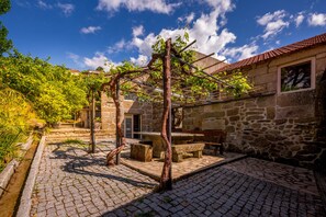 Un bâtiment en pierre doté d’une cour, d’une pergola et d’un banc en pierre.
