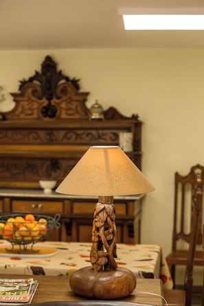 Una lámpara de mesa con base de madera y pantalla decorativa, un cuenco de naranjas y un piano al fondo.