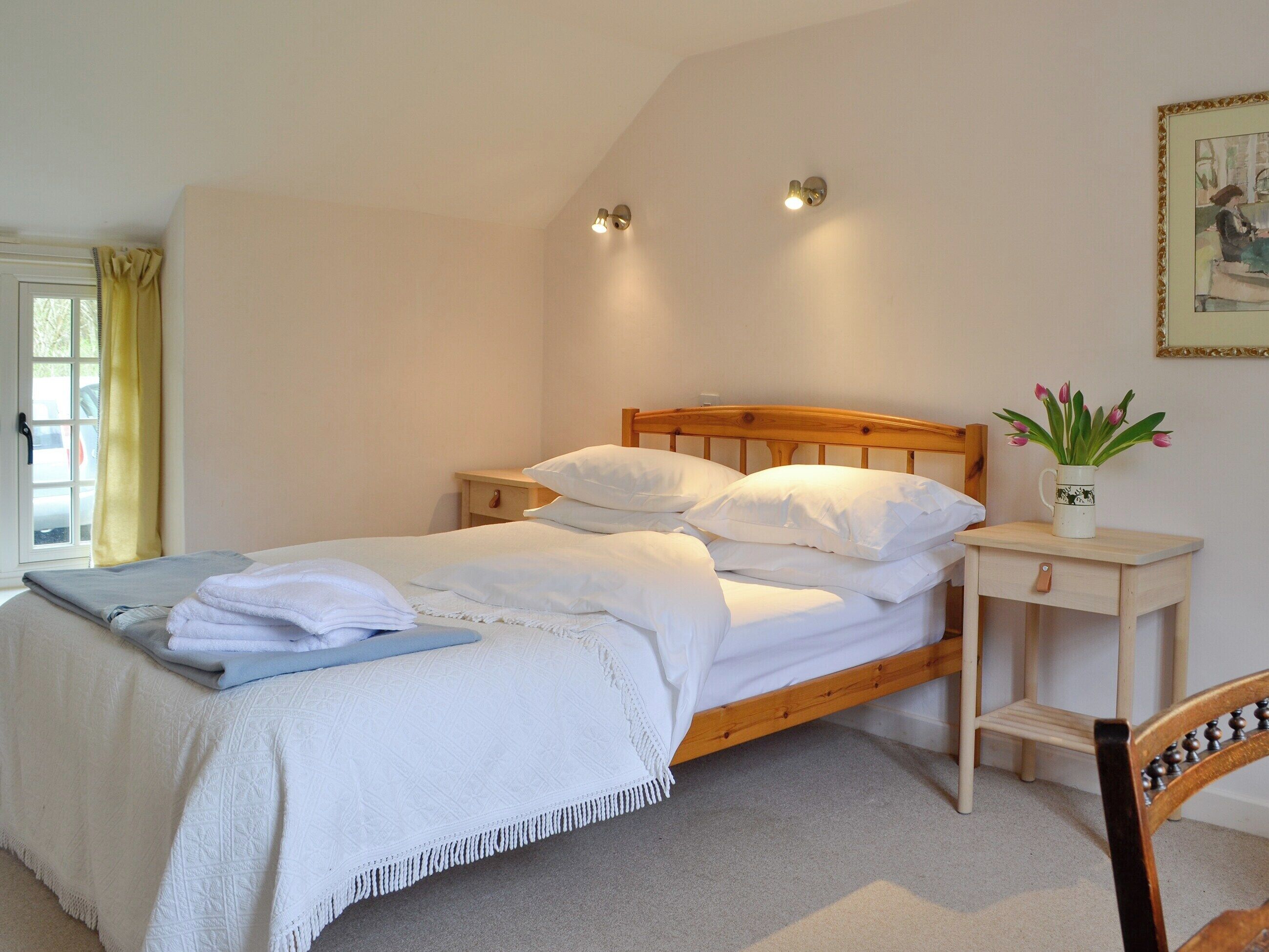 A neatly made bed with white linens, a bedside table with a lamp, and a small plant on a nightstand.