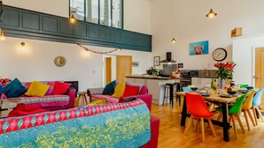 A spacious living area with a high ceiling, a kitchen with modern appliances, and a dining area with colorful chairs. - 4 bedroom accommodation in Hindolveston, near Holt (Hindolveston, near Holt)