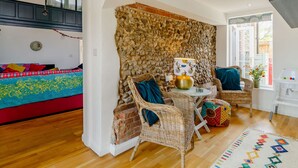 A room with a stone wall, a sofa with colorful cushions, wicker chairs, a small table with a vase, and a view of the outside. - 4 bedroom accommodation in Hindolveston, near Holt (Hindolveston, near Holt)