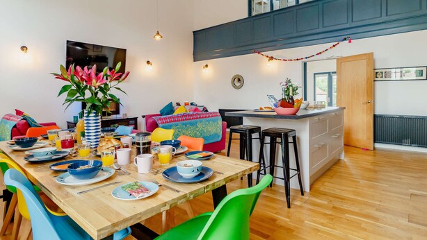 A dining area with a wooden table, colorful chairs, and a large vase of flowers. - 4 bedroom accommodation in Hindolveston, near Holt (Hindolveston, near Holt)