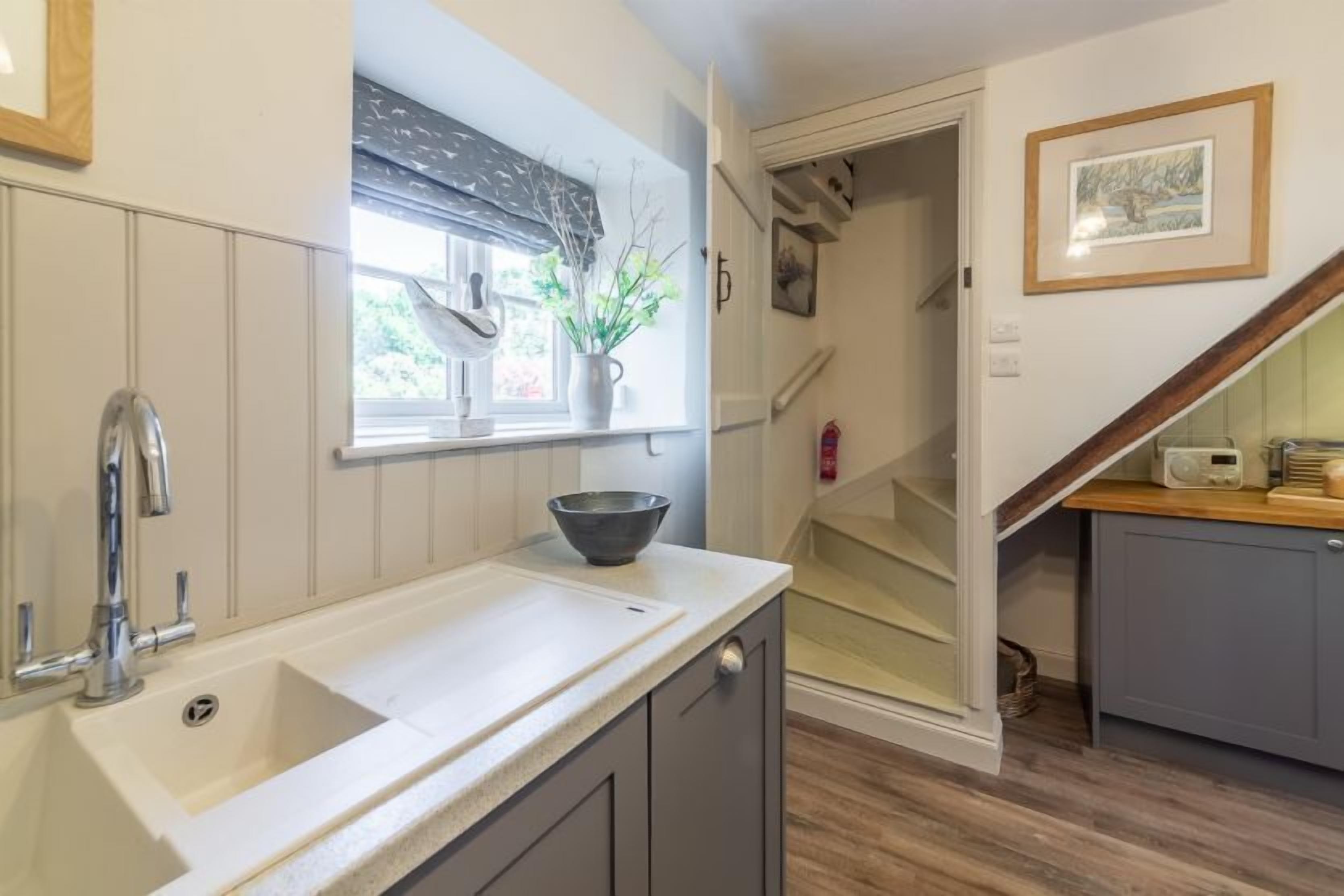 A kitchen with a sink, window, and a staircase leading to another room.