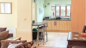A living room with a sofa, a dining table with chairs, a kitchen area with a microwave, and a window with a view. - 1 bedroom accommodation in Malvern (Malvern)
