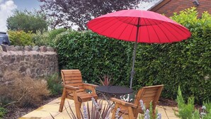 A patio with a table and two chairs, a red umbrella, and a hedge in the background. - 1 bedroom accommodation in Malvern (Malvern)