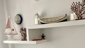 A room with a bed, pillows, a shelf with decorative items including a model sailboat, a lantern, and a starfish.