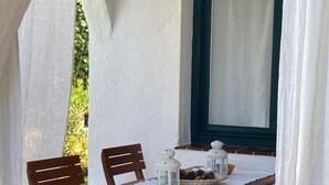 A wooden table with chairs, a white tablecloth, and decorative lanterns on a patio with a view of greenery.