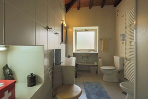 A bathroom with a toilet, sink, mirror, and a red medical kit.