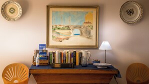 A room with a painting of a coastal scene, a bookshelf with books, a lamp, and two chairs. - Lemon Tree at Terrus Winery (Barrô, Viseu)