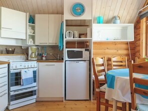 A compact kitchen with a stove, oven, microwave, and refrigerator. There is a sink with a faucet, a clock on the wall, and a dining table with chairs. - Etelätuuli by Interhome (Manamansalo)