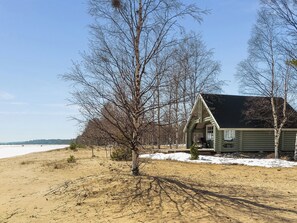 A cabin with a porch, surrounded by trees and a sandy beach.