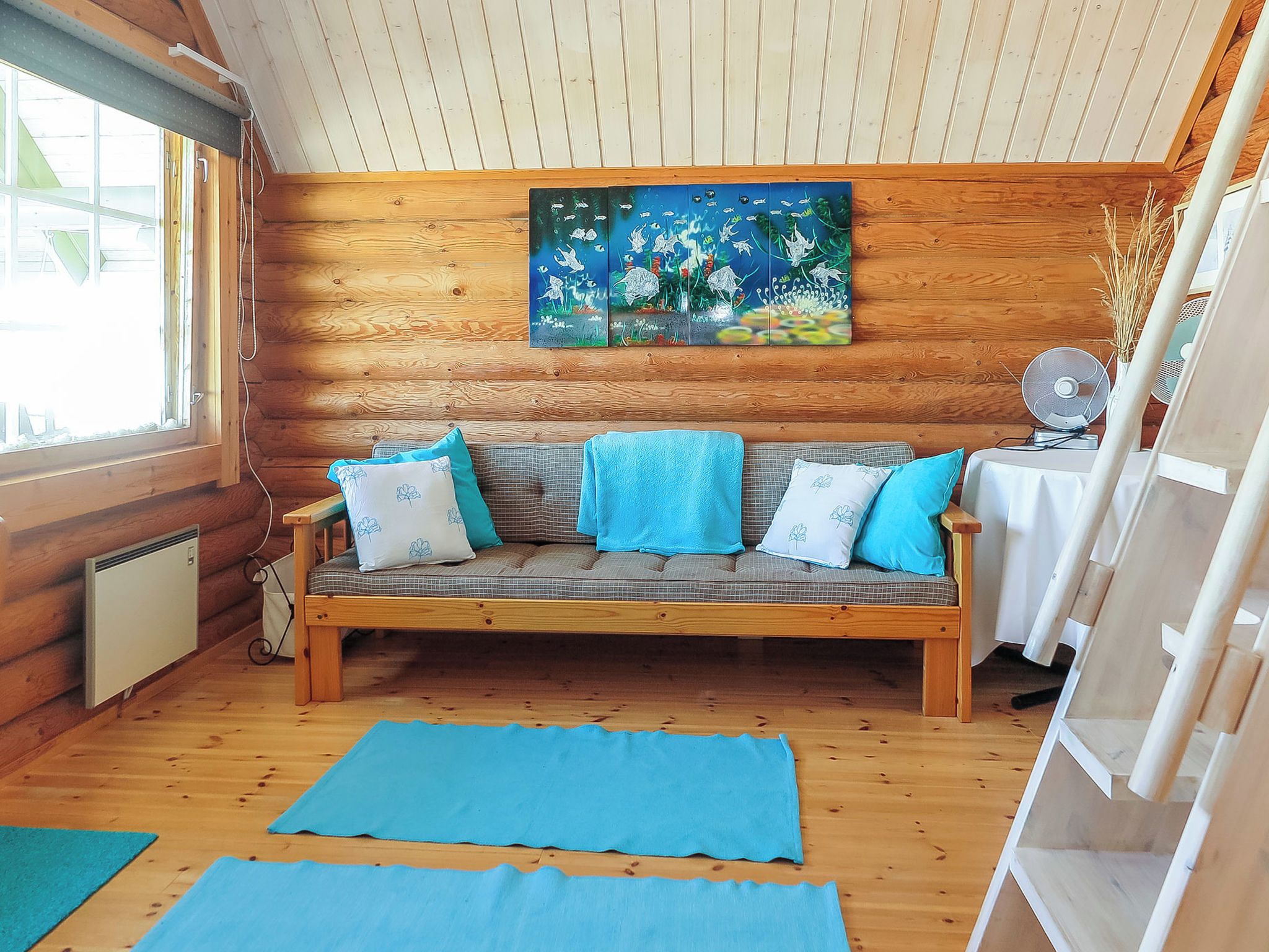 Ein Interieur einer Holzhütte mit einer Couch, Kissen, einem Gemälde und einem Ventilator.