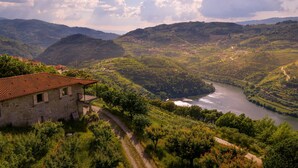 A stone building with a red-tiled roof, a river, and surrounding greenery. - River View at Terrus Winery (Barrô, Viseu)