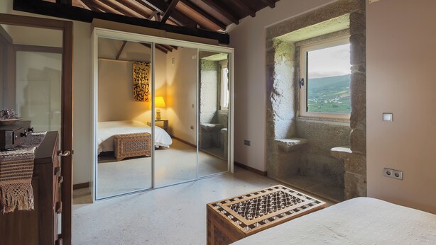 A bedroom with a bed, a bedside table, a lamp, a window with a view, and a sliding door leading to another room. - River View at Terrus Winery (Barrô, Viseu)
