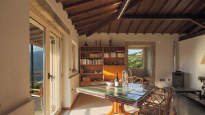A room with a wooden ceiling, a large bookshelf, a table with a colorful tablecloth, and a view of the outdoors. - River View at Terrus Winery (Barrô, Viseu)