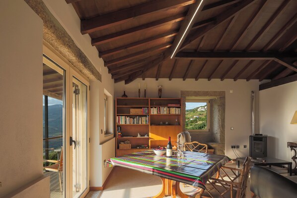 A room with a wooden ceiling, a large bookshelf, a table with a colorful tablecloth, and a view of the outdoors.