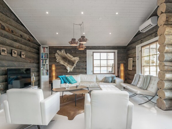 L’intérieur d’une cabane en rondins, avec un canapé blanc, un téléviseur, une bibliothèque et un grand tapis en fourrure.