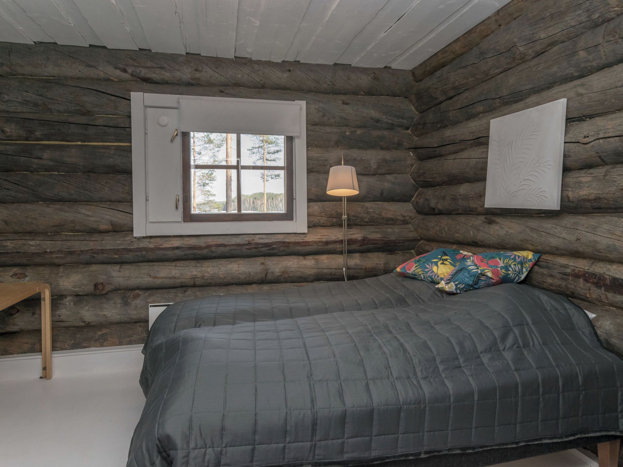 Une chambre à coucher située dans une cabane en rondins, avec un lit, une fenêtre et une lampe.