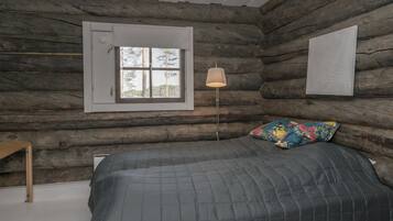 Een slaapkamer in een blokhut met een bed, een raam en een lamp.