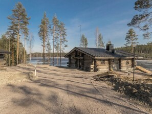 Una cabana de fusta amb teulada metàl·lica, envoltada per un bosc i una massa d'aigua.