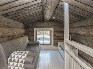 L’intérieur d’une cabane en rondins, avec un plafond en bois, un canapé recouvert d’un plaid à motifs et une fenêtre donnant sur la forêt.