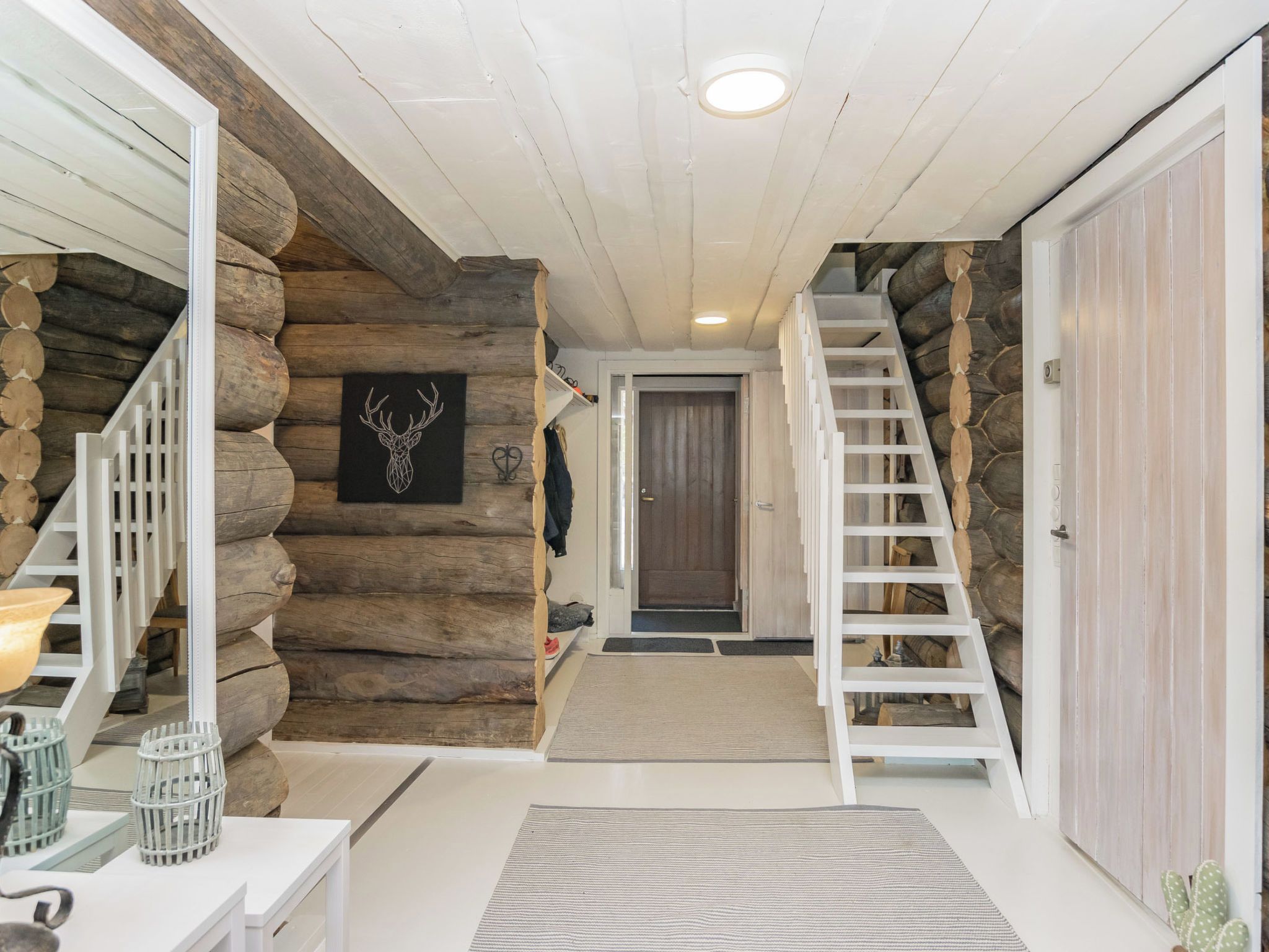 Een houten blokhut interieur met een trap, een houten deur en een decoratie van een gestileerde hertenkop.