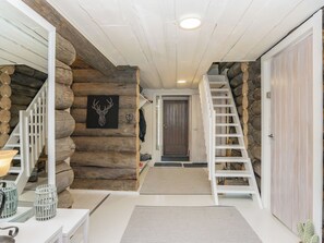 Een houten blokhut interieur met een trap, een houten deur en een decoratie van een gestileerde hertenkop.