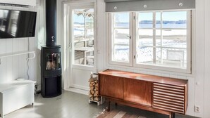 Une pièce avec une cheminée, un téléviseur, un banc et une grande fenêtre donnant sur un paysage enneigé.
