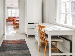 A modern, well-lit room with a white desk, wooden chair, and a large window.