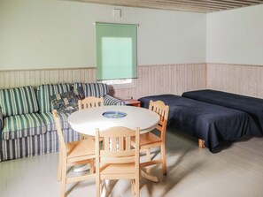 A room with a striped sofa, a round table with chairs, and two beds.