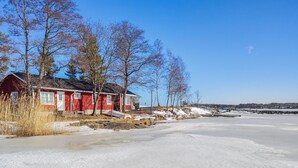 Une maison en bois rouge, dotée d’un porche, entourée de neige et d’arbres.