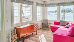Une pièce chaleureuse avec un banc en bois, un canapé rouge et un fauteuil. De grandes fenêtres offrent une vue sur un paysage enneigé.