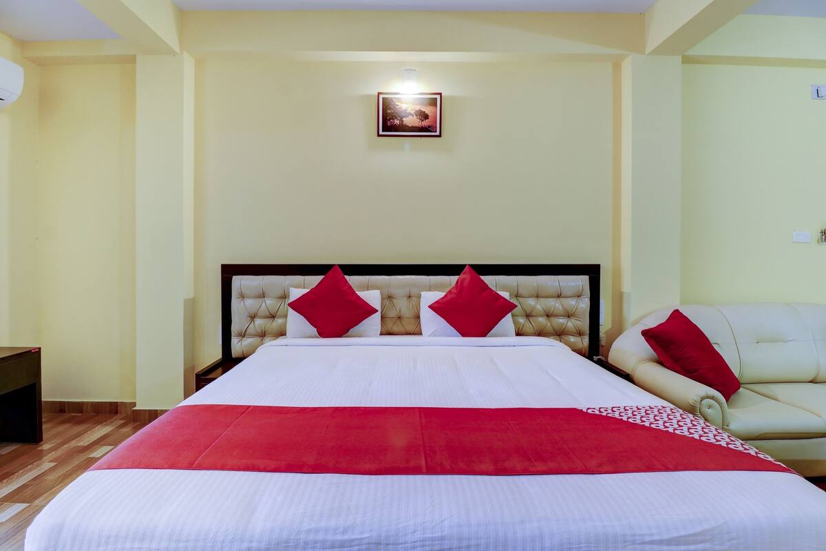 Ett hotellrum med en stor säng, en sänggavel med knäppning och ett rött och vitt sängöverkast.