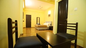 A room with a bed, a bedside table, a chair, and a table. - Gaurika Residency Lodging and Boarding (Udupi)