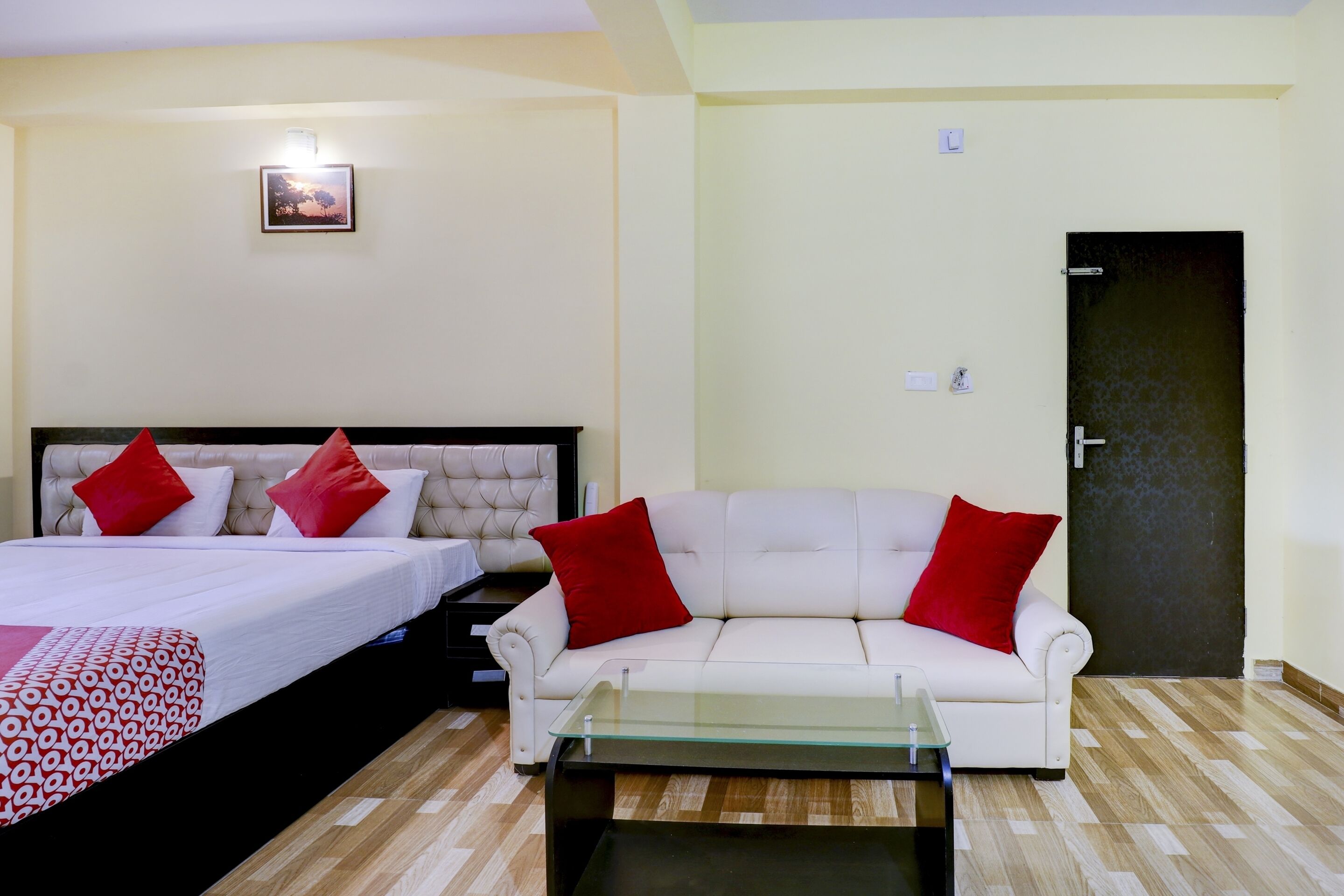 Una habitación de hotel con una cama, un sofá blanco, una mesa de centro de vidrio y una puerta.