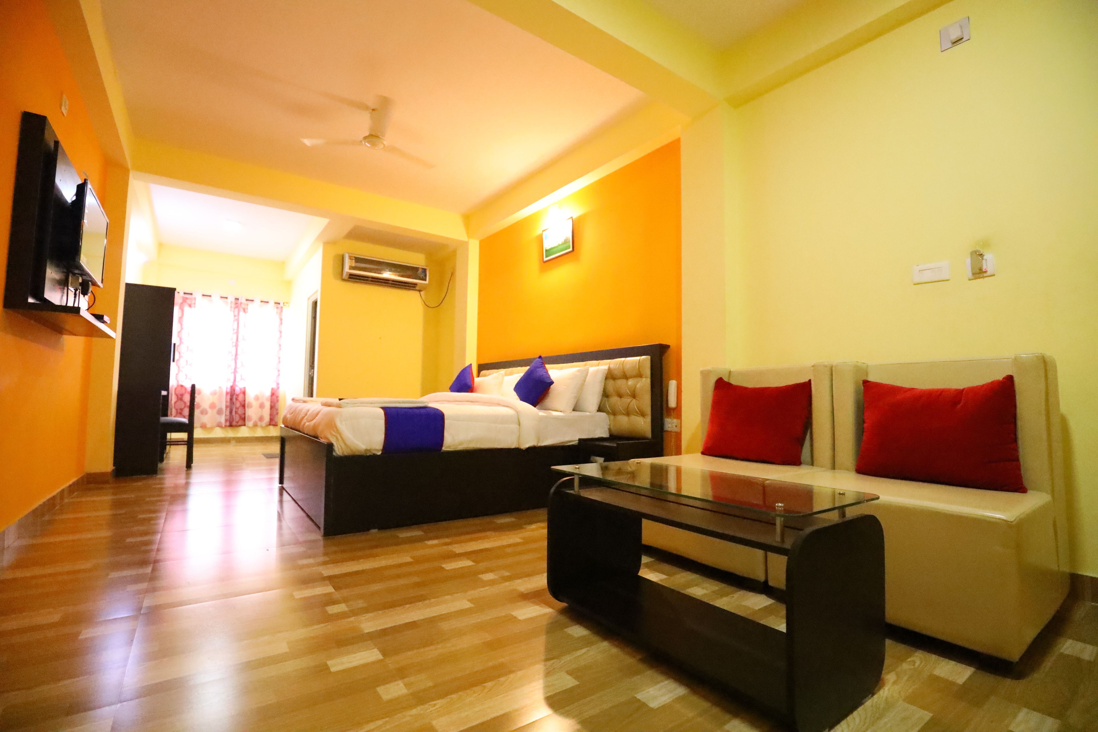 A hotel room with a bed, a sofa, a glass coffee table, and a television.