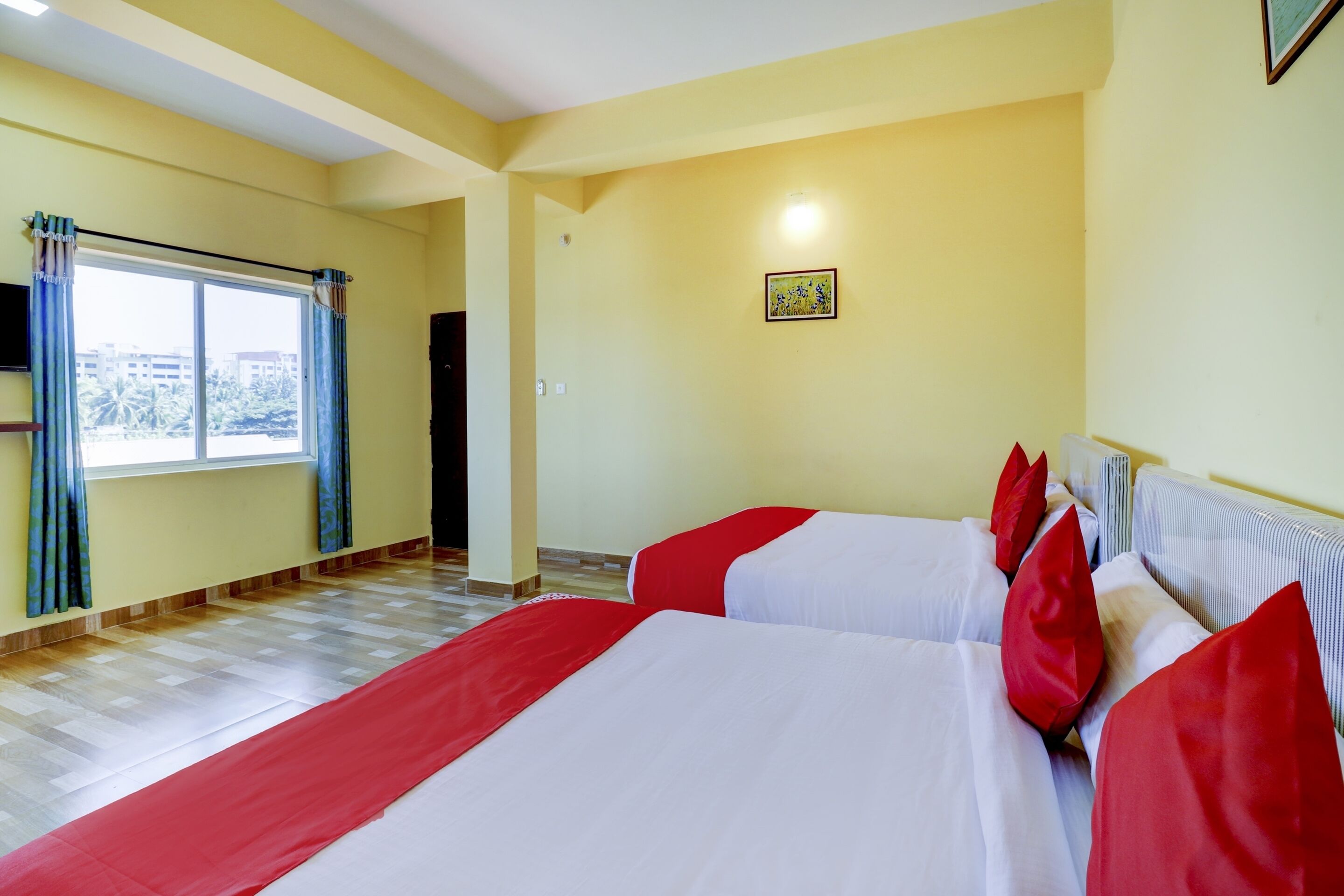 A hotel room with two beds, a window with curtains, a radiator, and a small painting on the wall.
