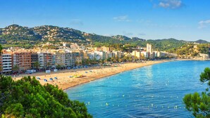Un paisaje costero con playa, edificios y montañas al fondo.
