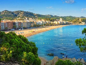 Paesaggio costiero con spiaggia, edifici e montagne sullo sfondo.