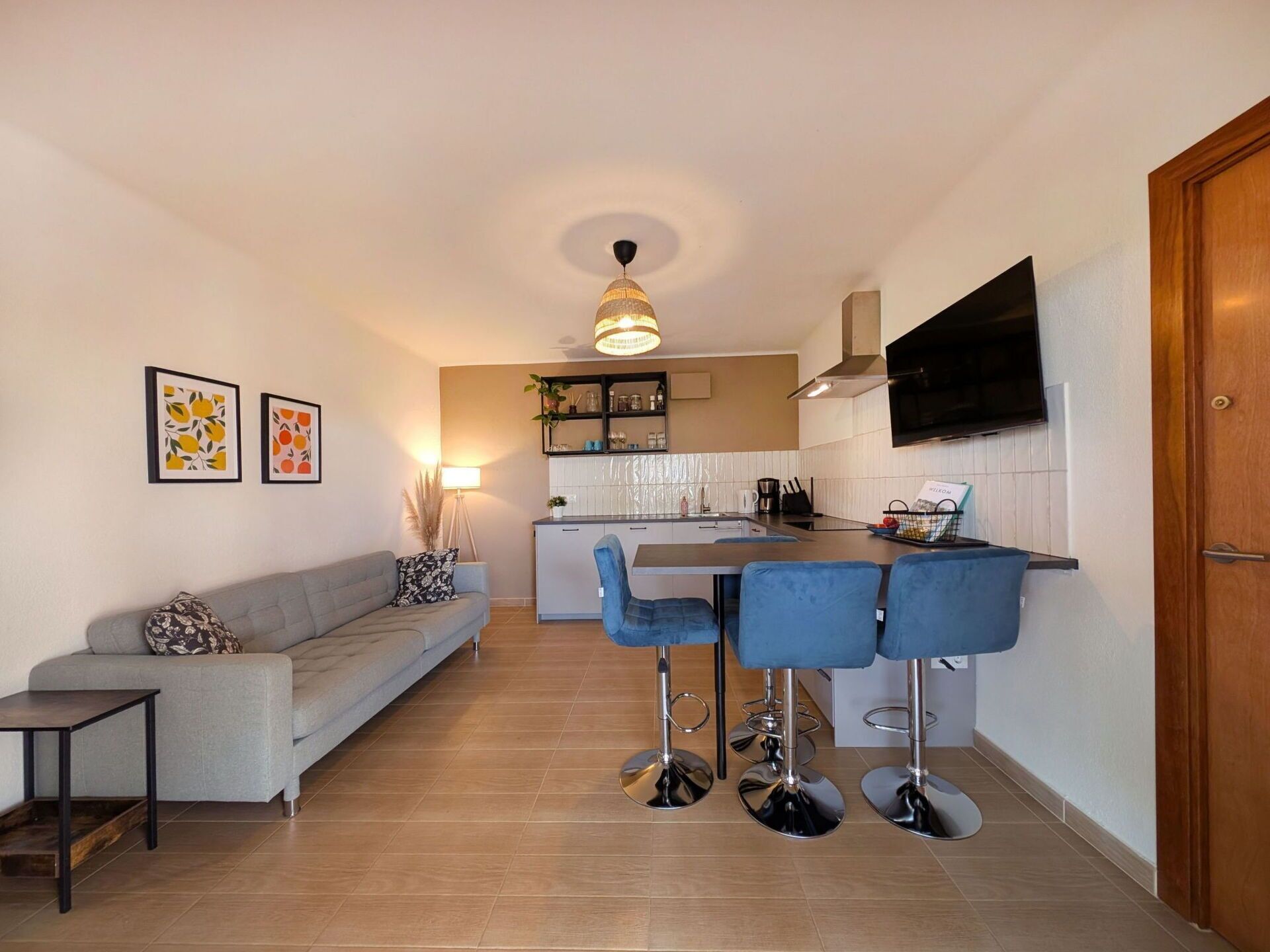 A modern kitchen with a central island, bar stools, a sofa, and a television mounted on the wall.