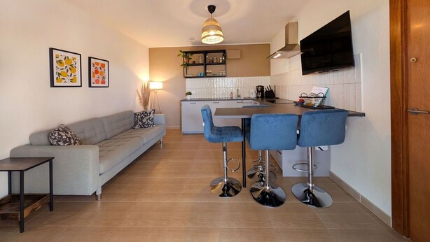 Una cocina moderna con una isla central, taburetes de bar, un sofá y un televisor montado en la pared.