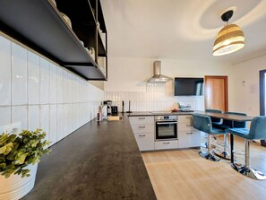 A modern kitchen with a dark countertop, white cabinets, a built-in oven, and a dining area with blue chairs.