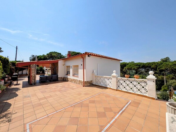 A residential property with a tiled patio, a covered outdoor seating area, and a white fence with decorative elements.